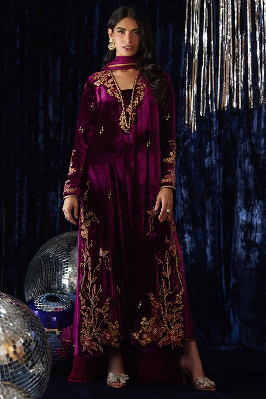 Woman in a burgundy embroidered dress standing against a dark background with decorative elements.