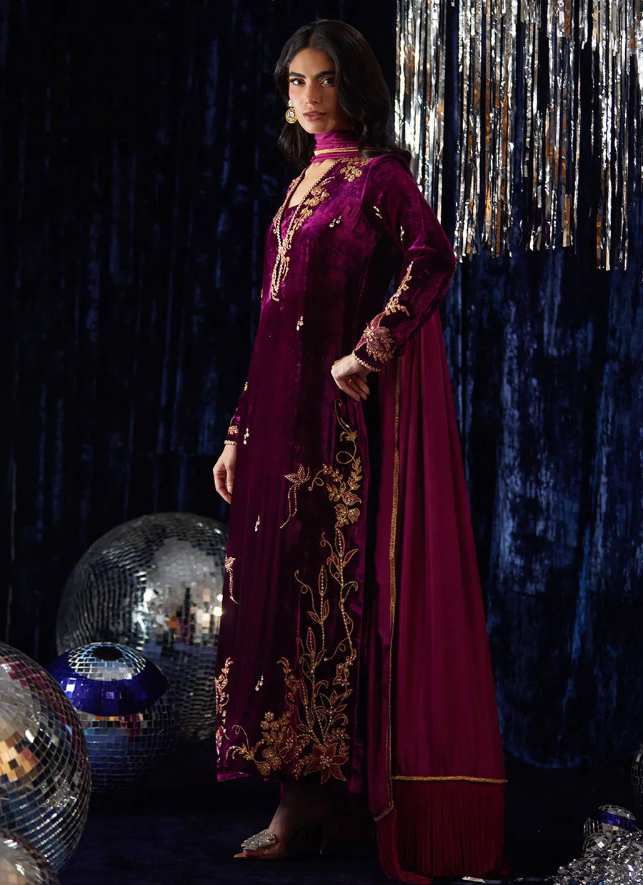 Woman in a burgundy embroidered dress standing against a dark background with disco balls.