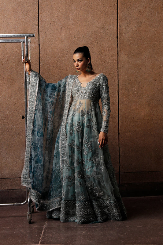 Woman in a long, elegant dress with a matching shawl against a brown wall.