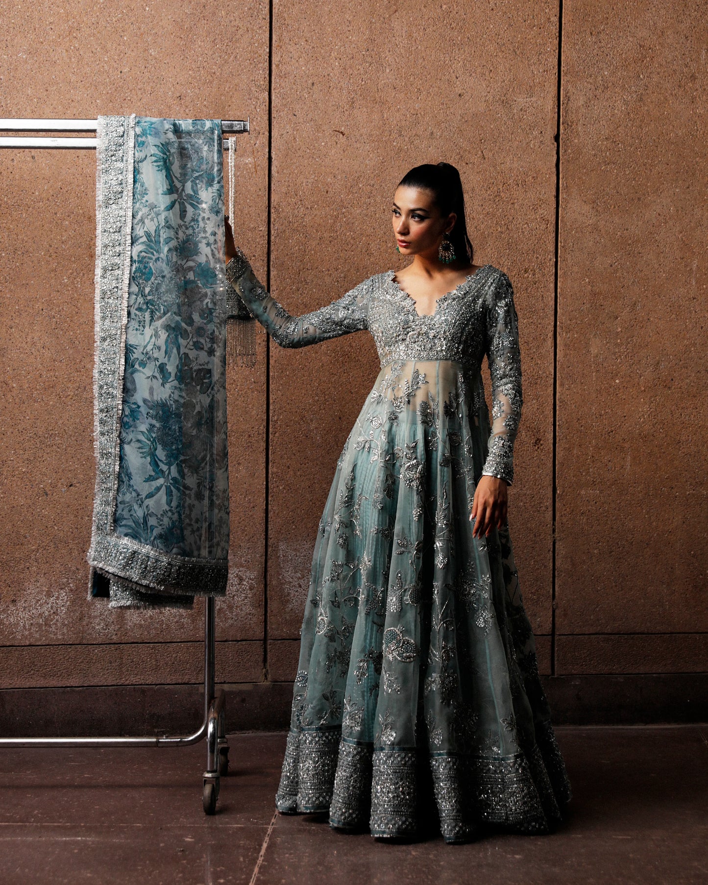 Woman in a long, elegant dress holding a matching shawl against a brown wall.