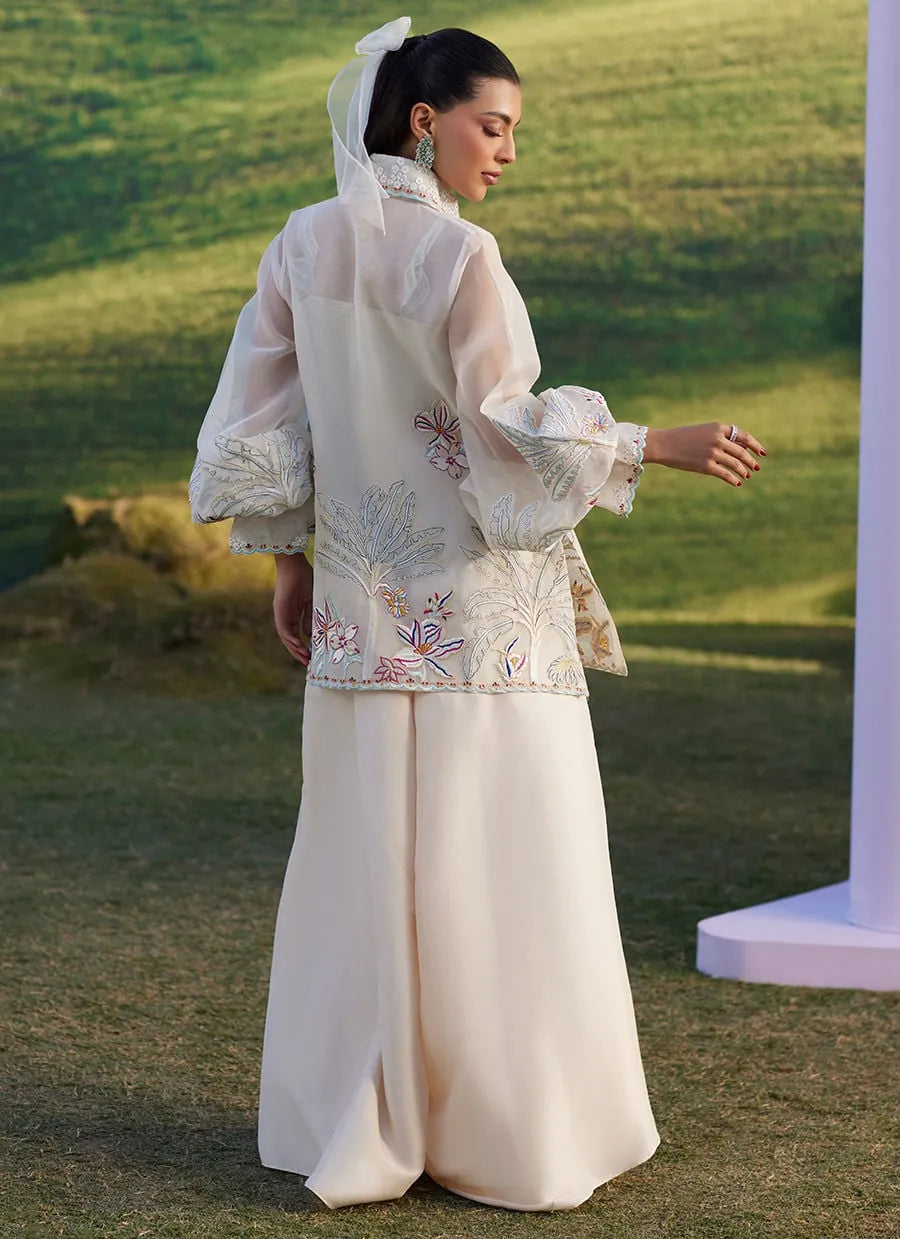 Woman in traditional embroidered outfit standing outdoors with green grass in the background