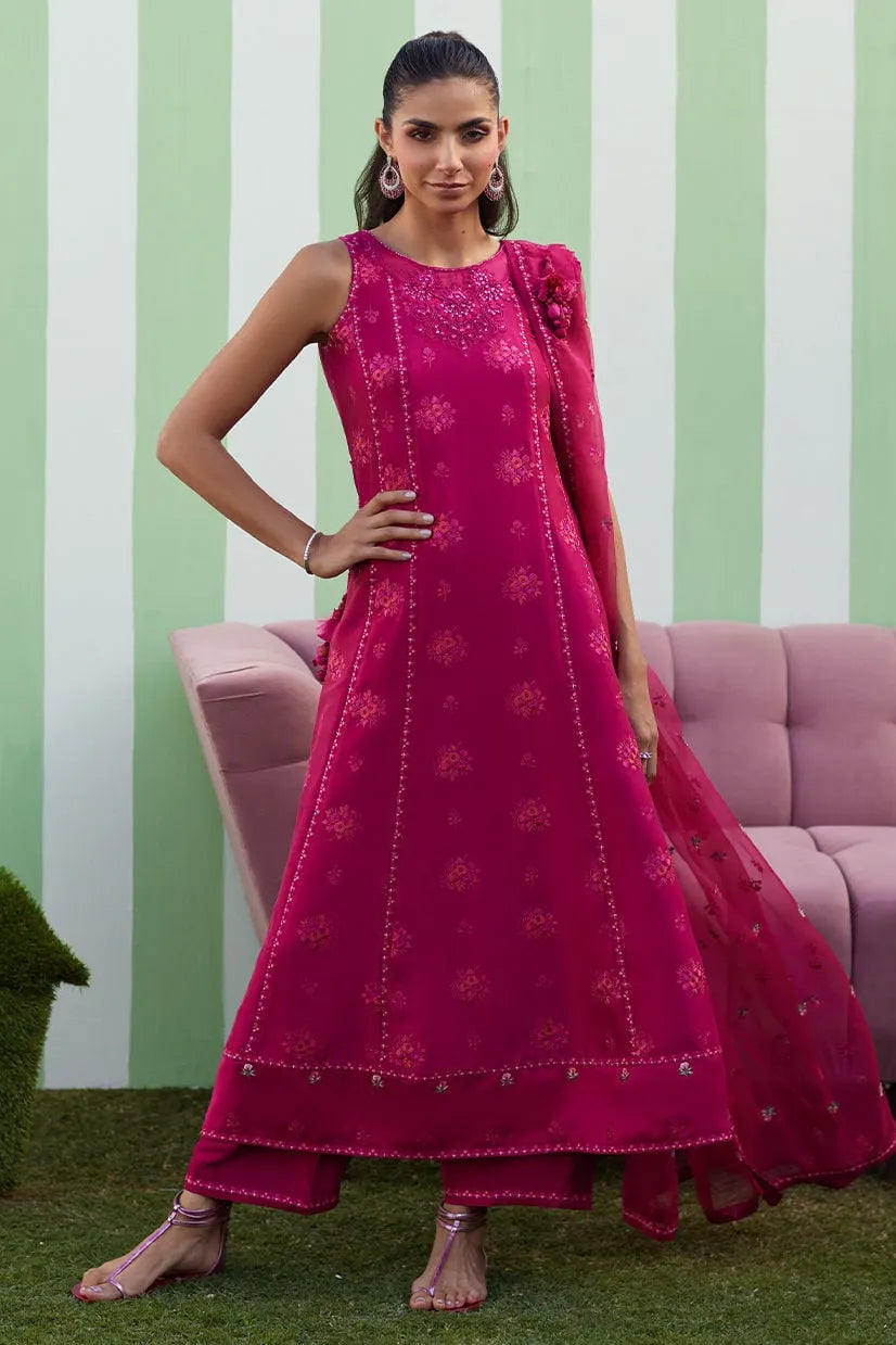 Woman in a pink traditional outfit standing in front of a striped wall with a pink couch.