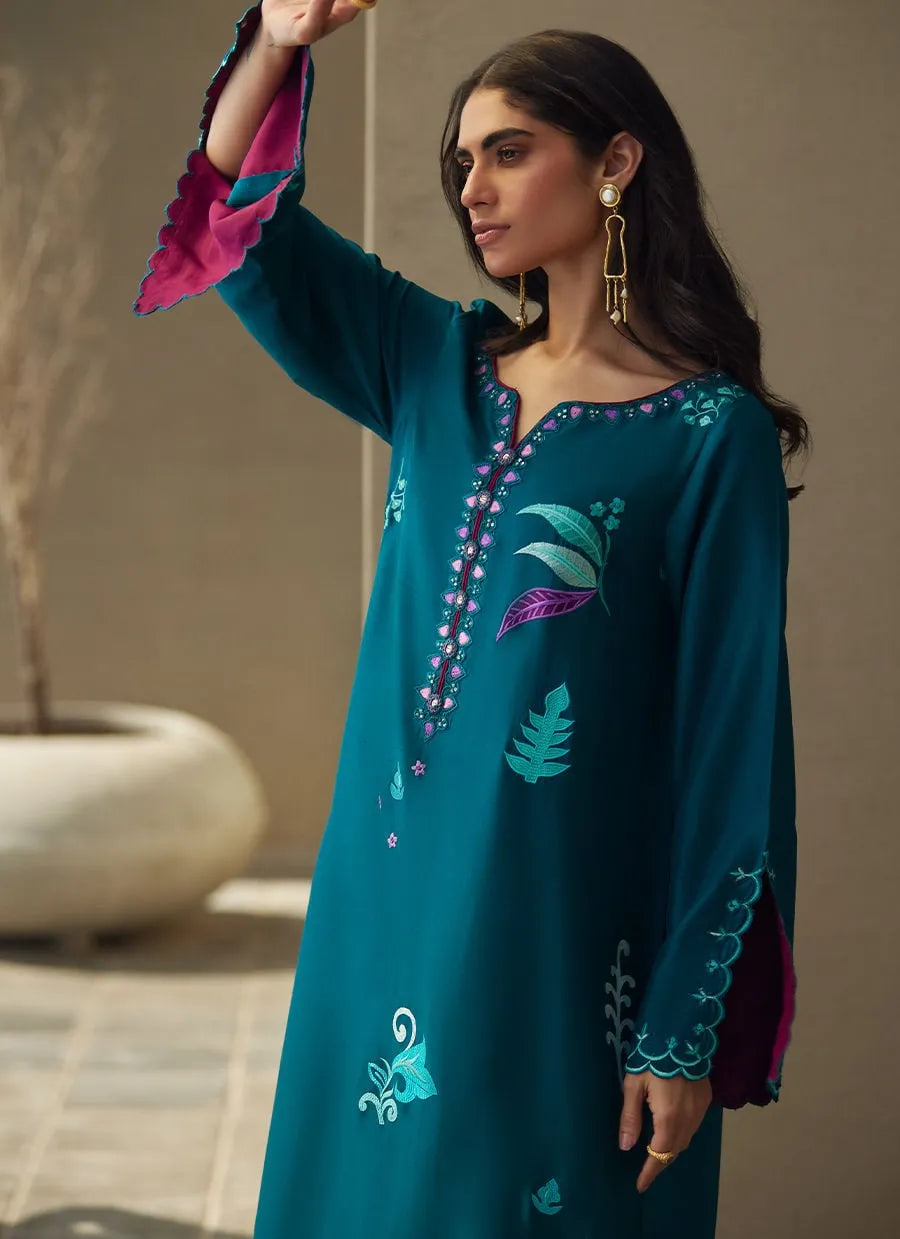 Woman wearing a teal embroidered dress with pink sleeves against a neutral background