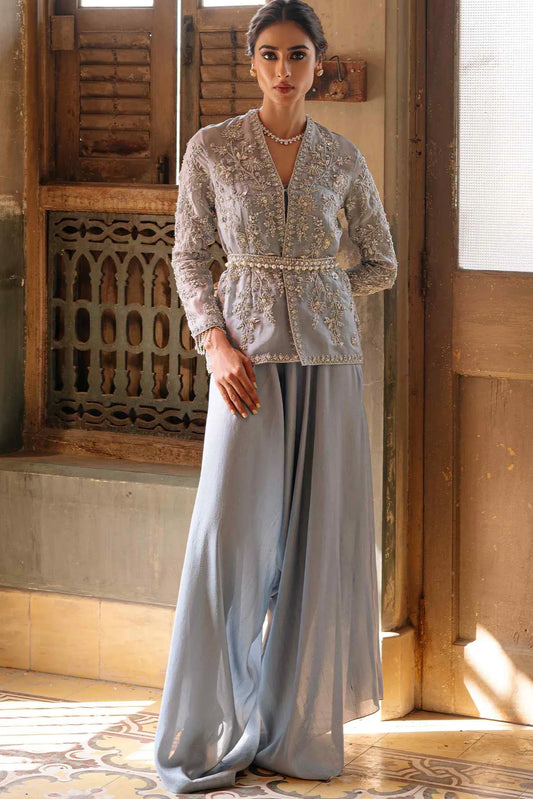 Woman wearing a light gray outfit with intricate detailing in a warm-toned interior setting.