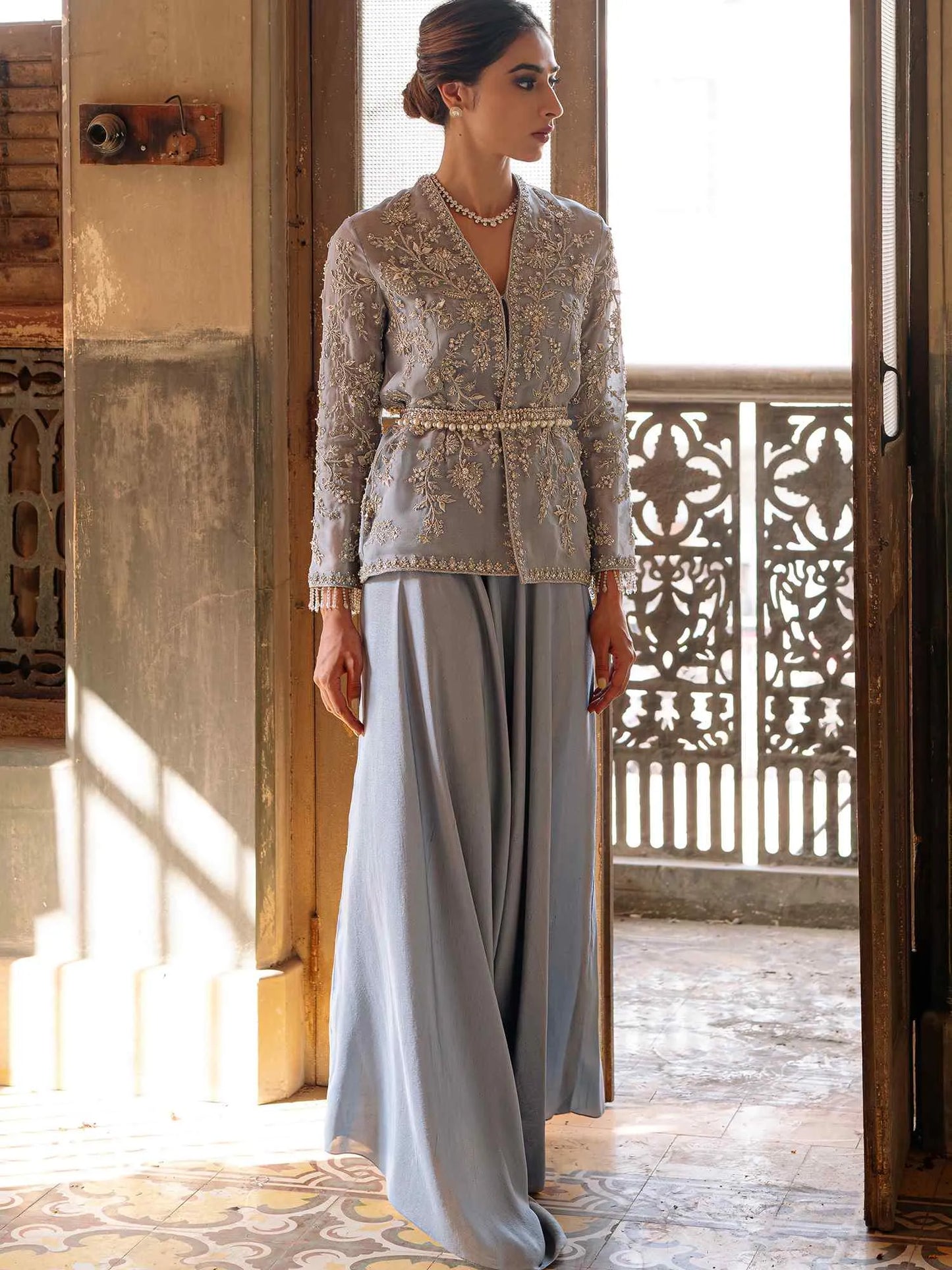 Woman in a gray outfit standing in a sunlit room with decorative elements.
