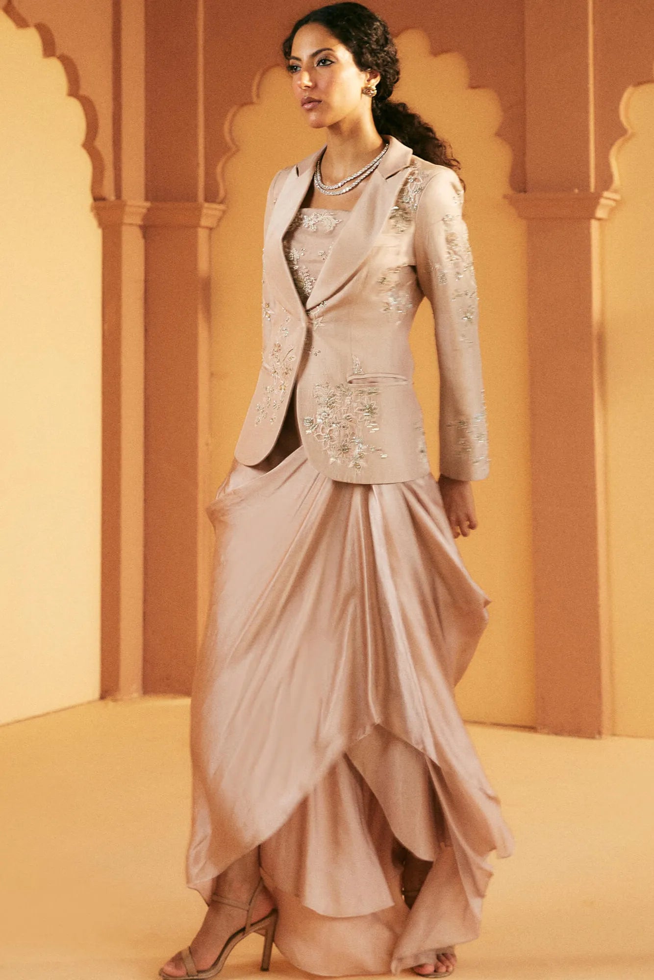 Woman wearing a traditional outfit with a jacket and drape skirt against an architectural background.