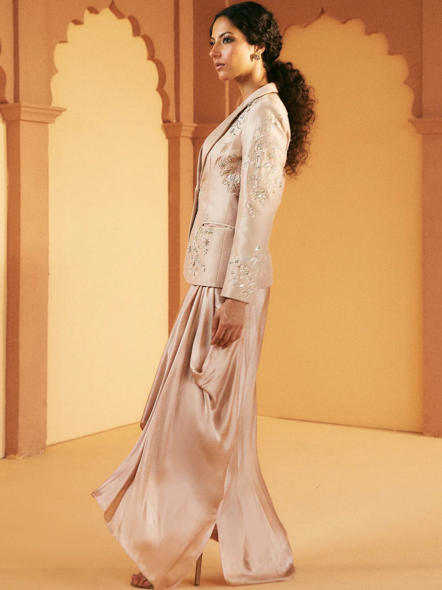 Woman in a traditional outfit standing against an ornate wall.