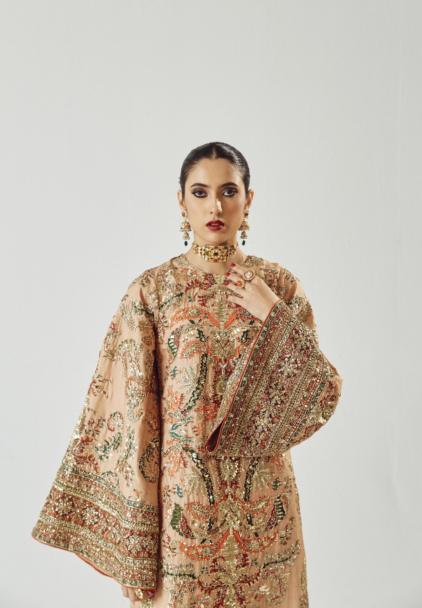 Woman wearing a traditional embroidered outfit with a plain background