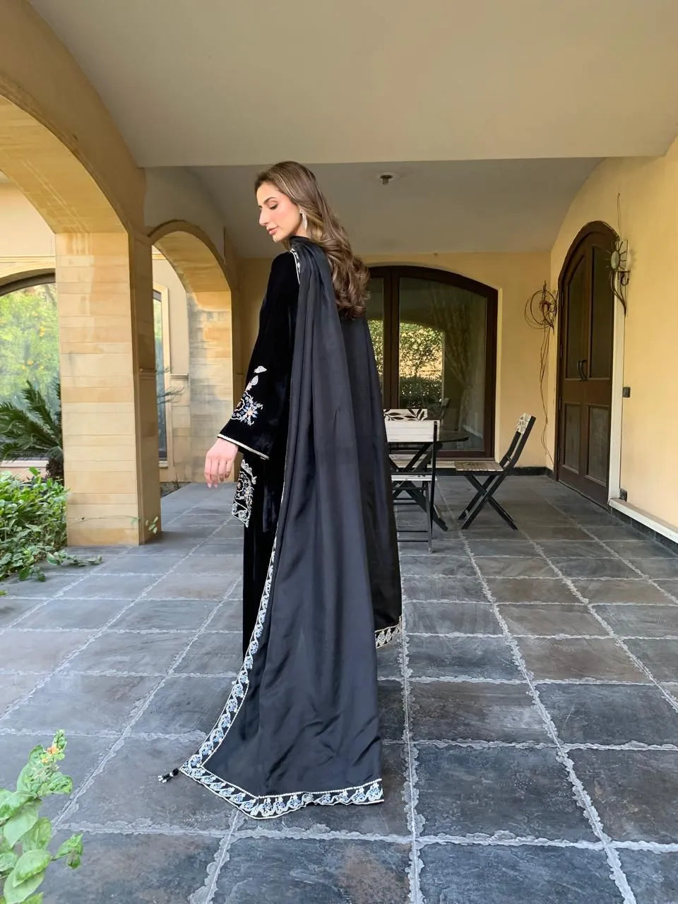 Woman in a black dress with white embroidery standing on a stone patio.