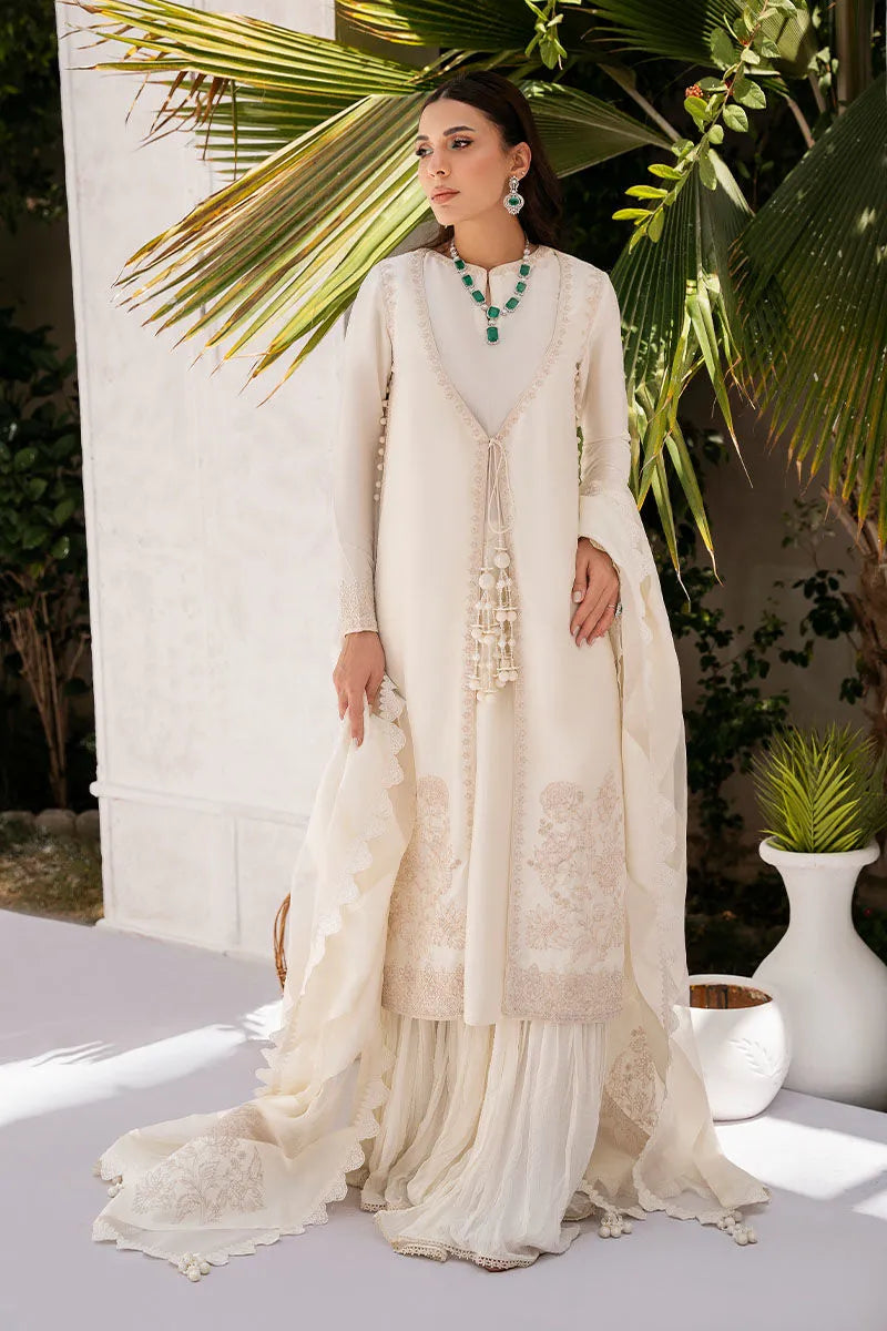 Woman in a cream-colored traditional outfit with green jewelry standing outdoors.