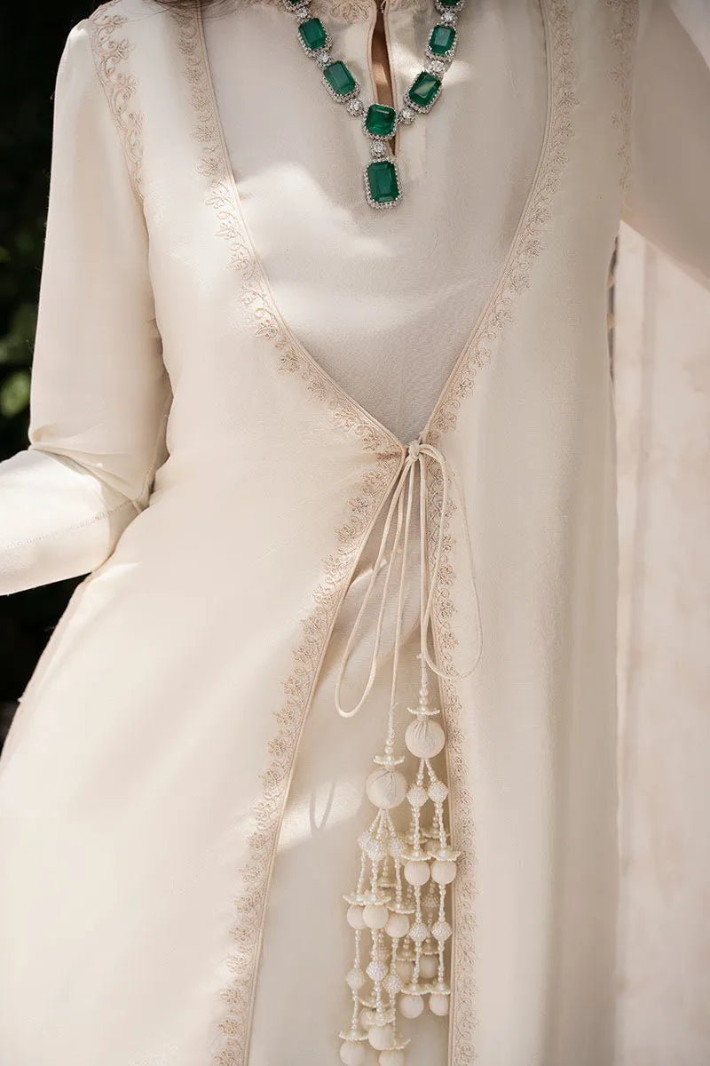 Close-up of a white dress with intricate detailing and a necklace with green gemstones.