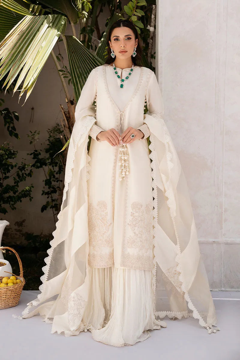Woman in a white traditional outfit standing against a neutral background with plants.