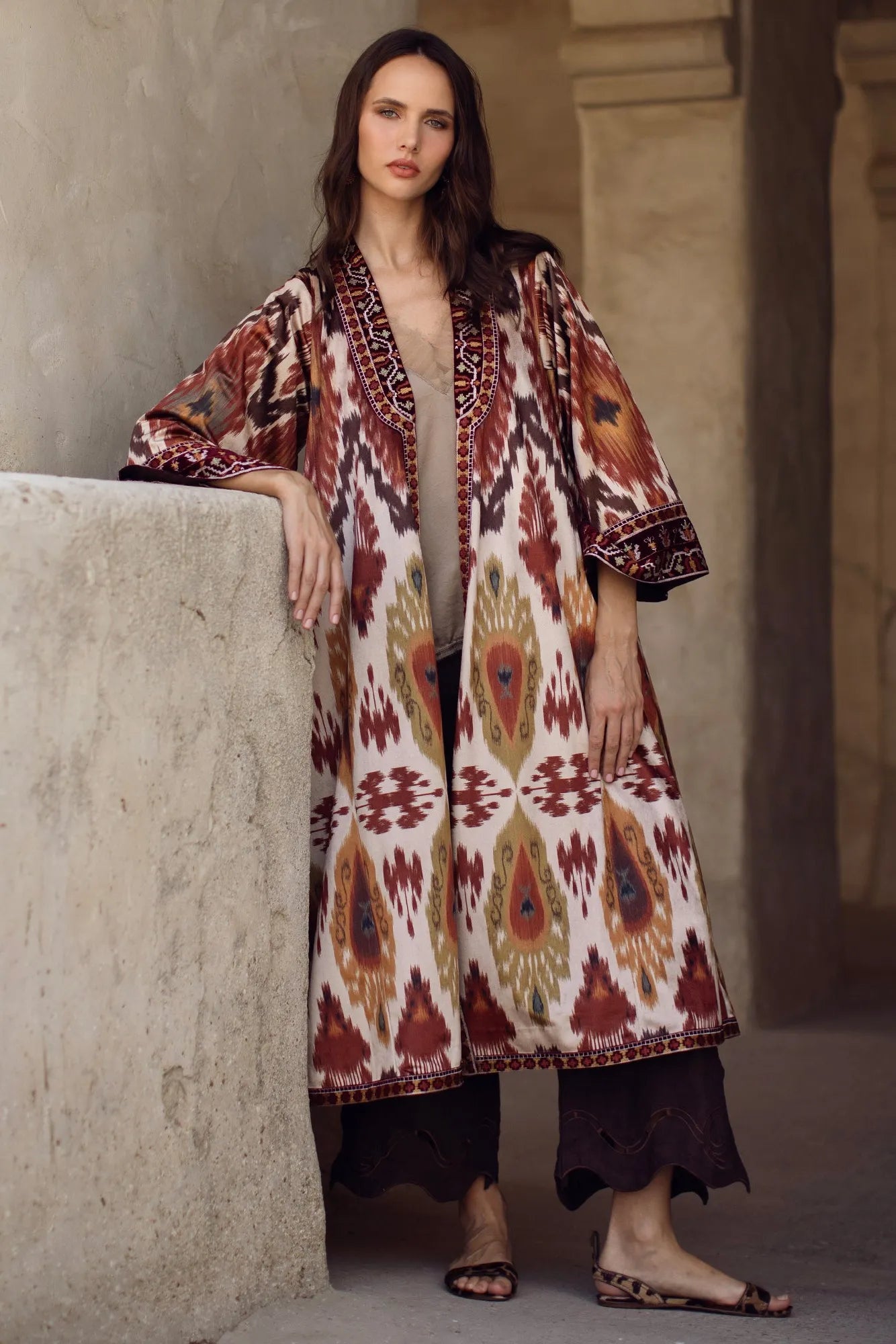 Woman wearing a patterned long coat standing against a neutral wall.