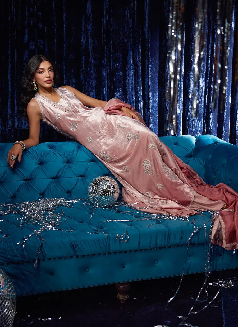 Woman in a pink dress lying on a blue couch with a disco ball and tinsel around, against a dark curtain background.
