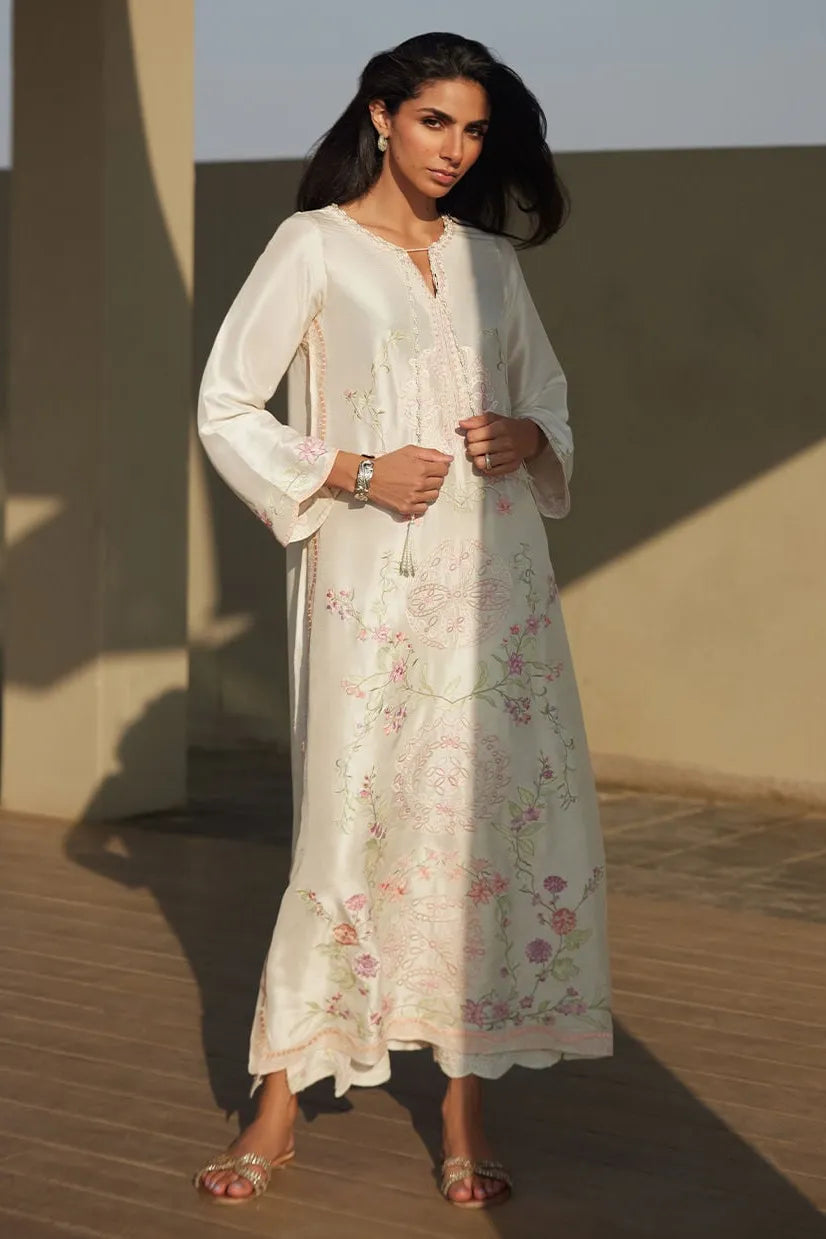 Woman wearing a white floral dress standing against a plain background