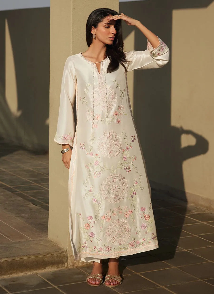 Woman wearing a long, light-colored dress with floral patterns against a neutral wall.