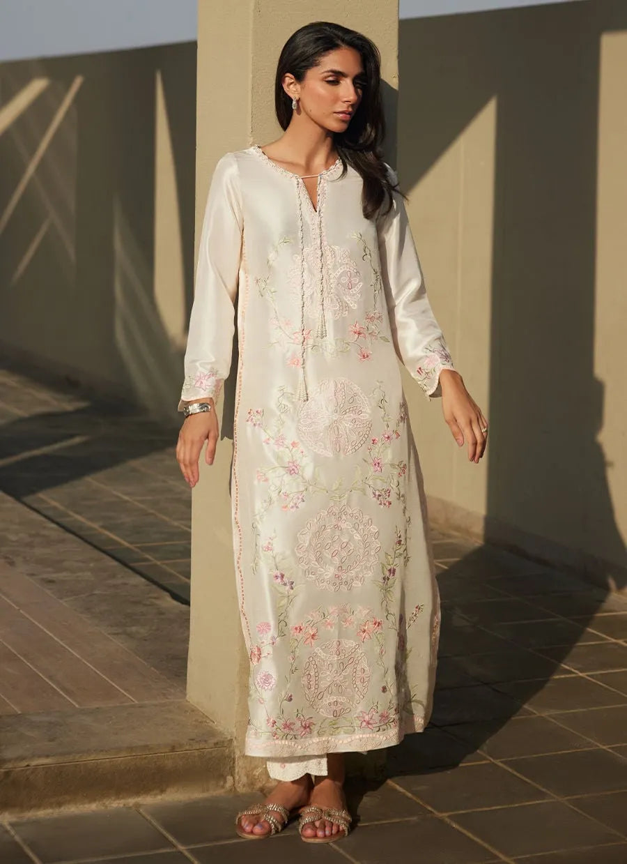 Woman wearing a floral dress standing against a wall with sunlight casting shadows.