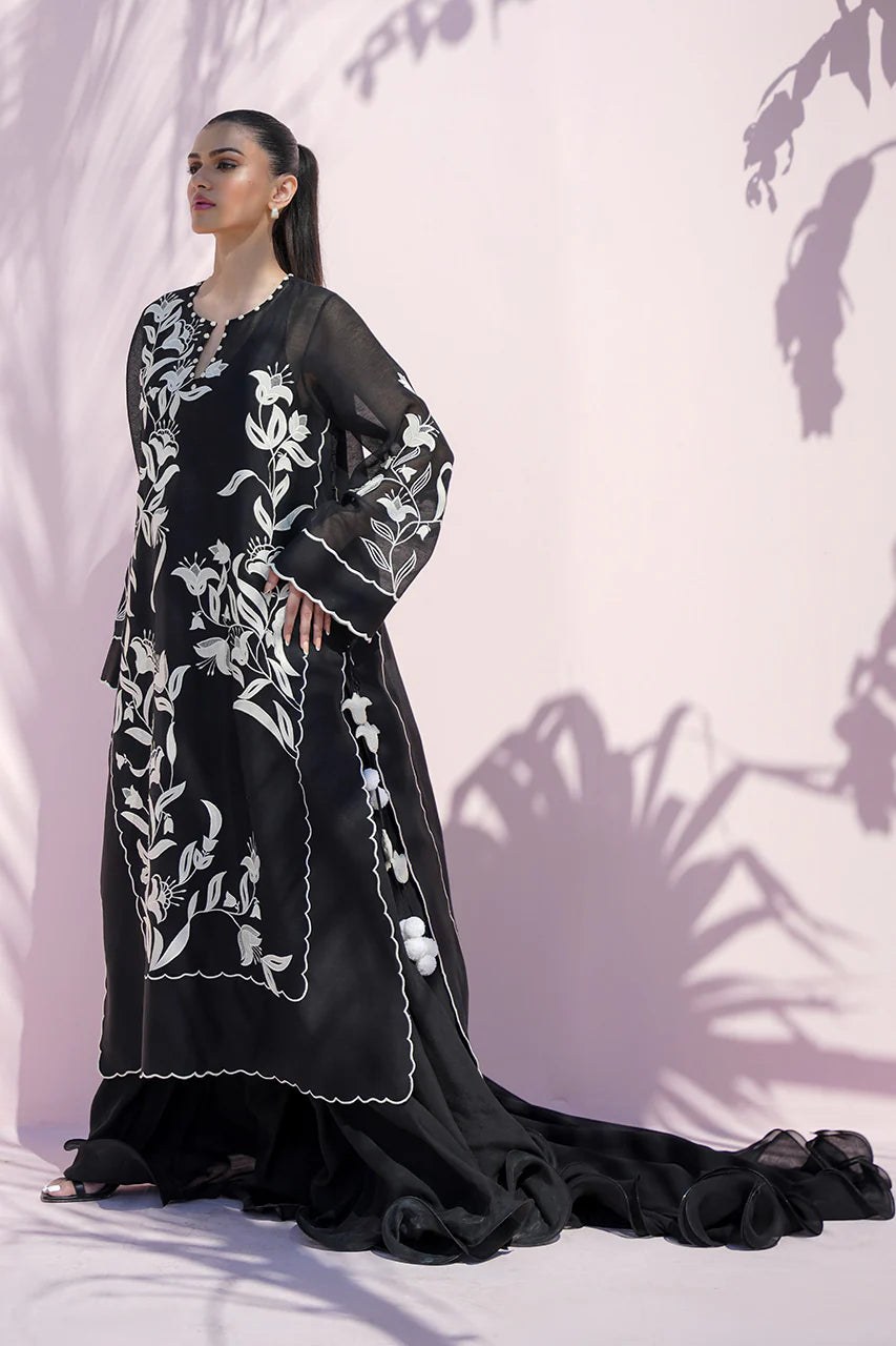 Woman wearing a black dress with white floral embroidery against a light pink background