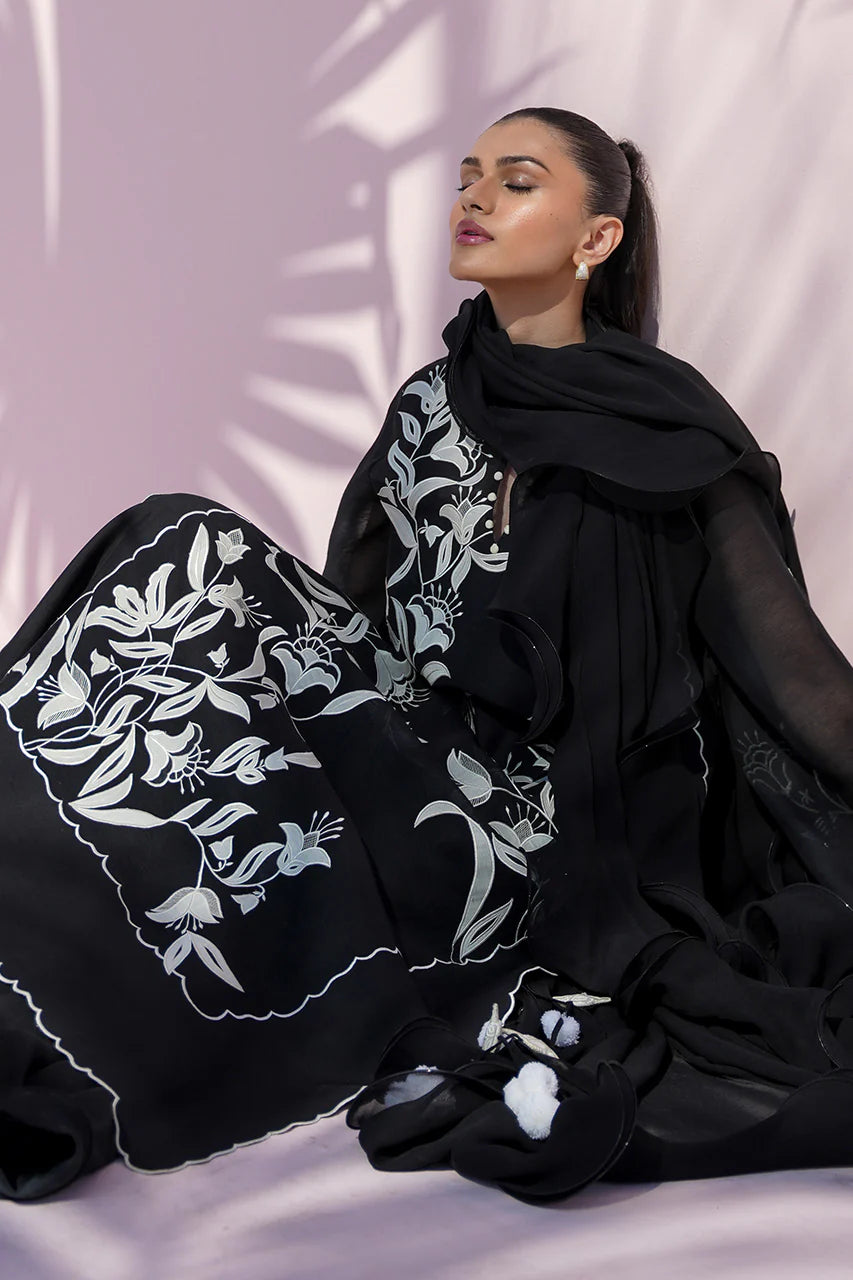 Woman wearing a black outfit with white floral patterns against a light pink background