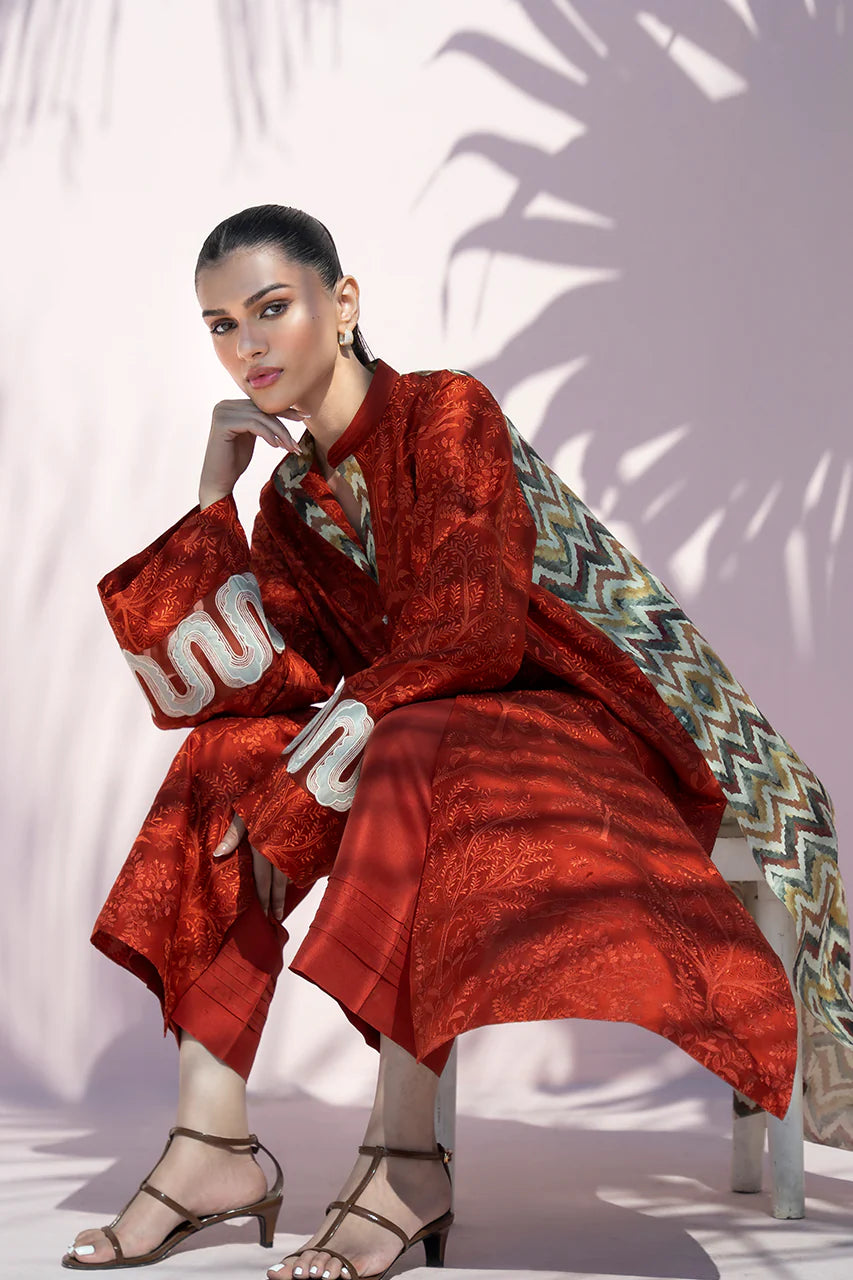 Woman in a red outfit with a patterned scarf sitting on a white stool against a light pink background.