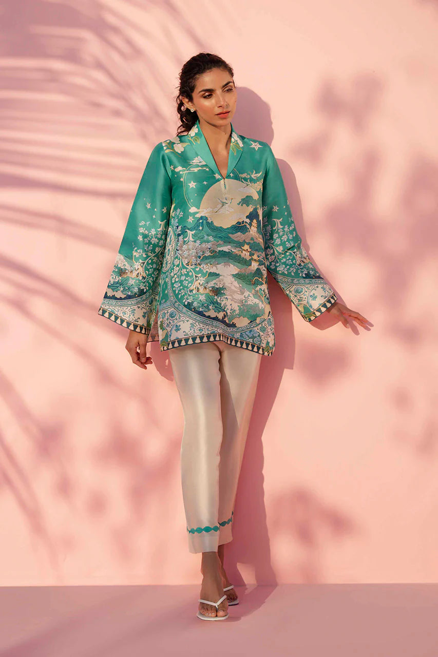 Woman wearing a teal floral blouse and white pants against a pink background