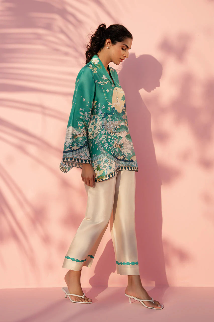 Woman wearing a teal floral blouse and white pants against a pink background