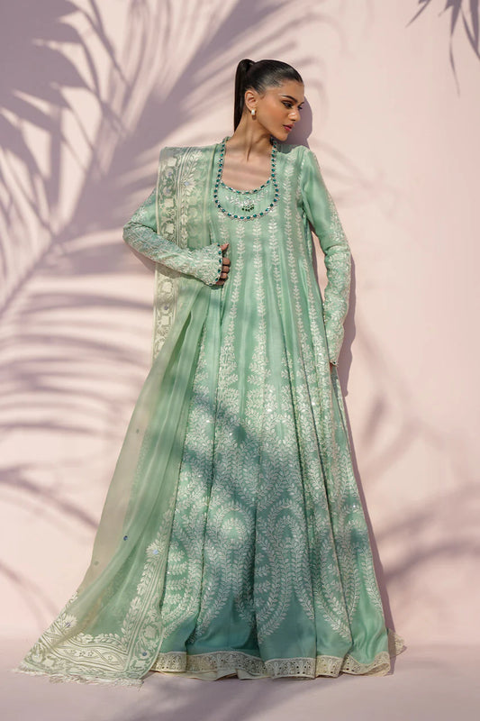 Woman wearing a light green embroidered traditional outfit against a pink background with leaf shadows.