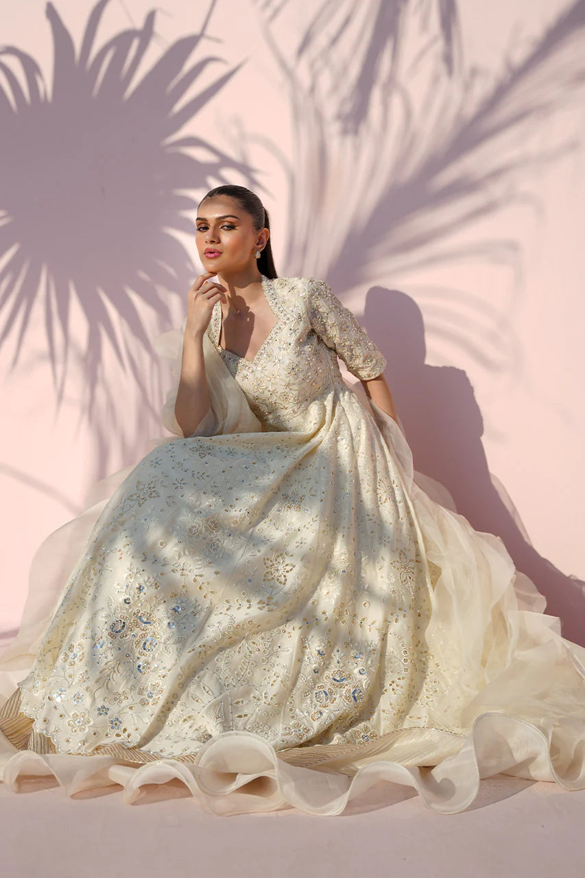 Woman in a white embroidered gown against a pink background with palm leaf shadows