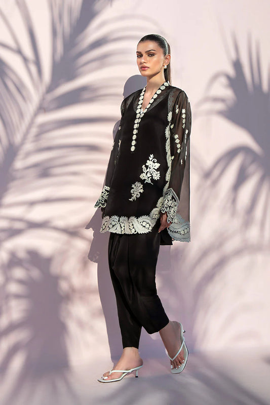 Woman wearing a black outfit with white embroidery against a textured wall.