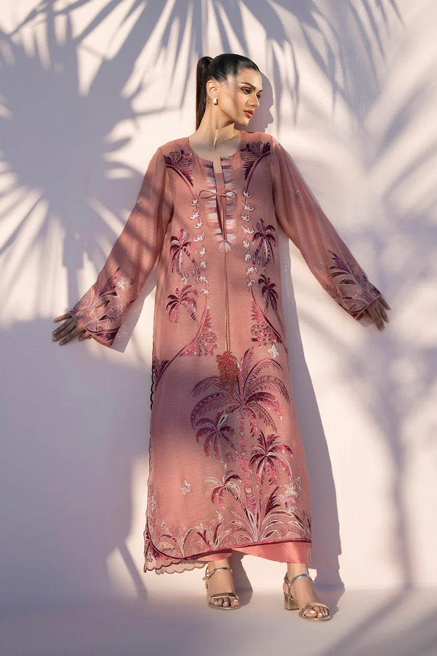 Woman wearing a pink embroidered dress with palm tree patterns against a white wall.