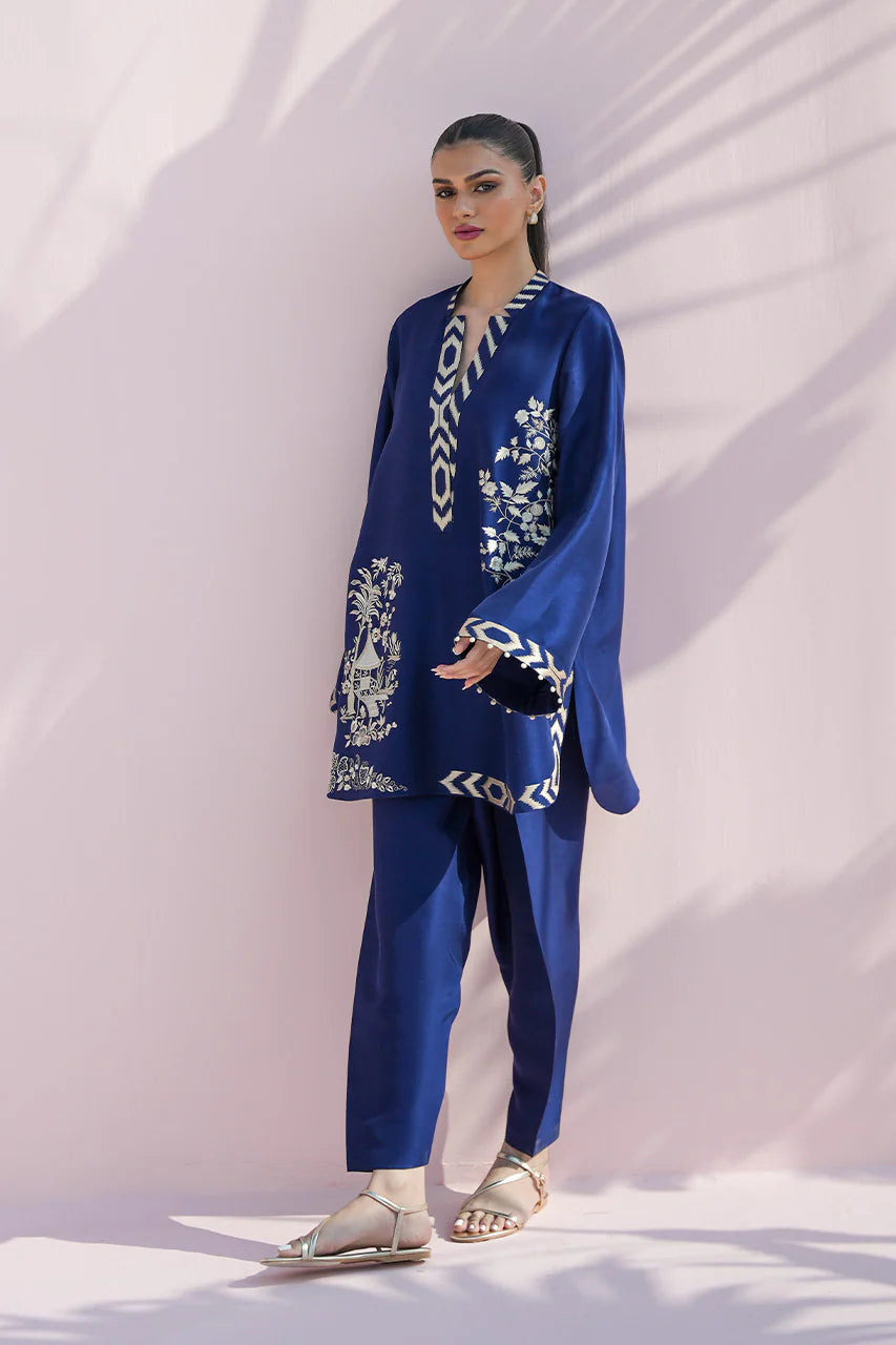 Woman wearing a blue embroidered outfit against a white background