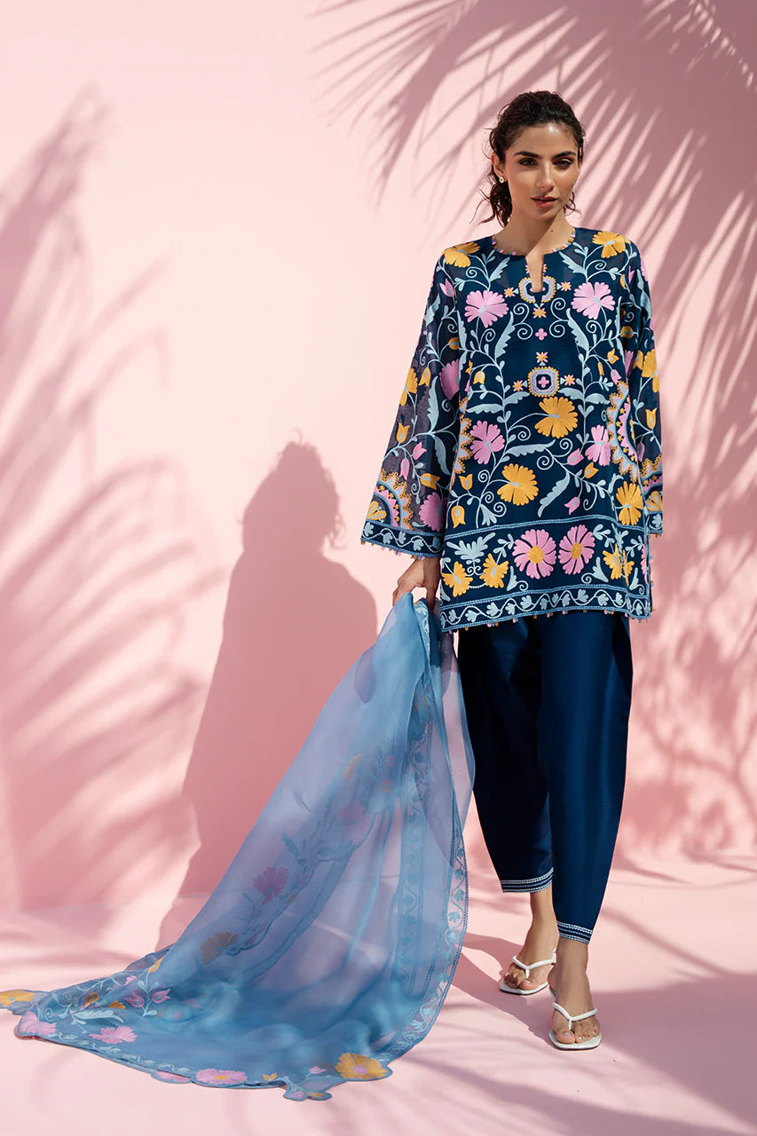 Woman in a floral embroidered outfit with a blue dupatta against a pink background