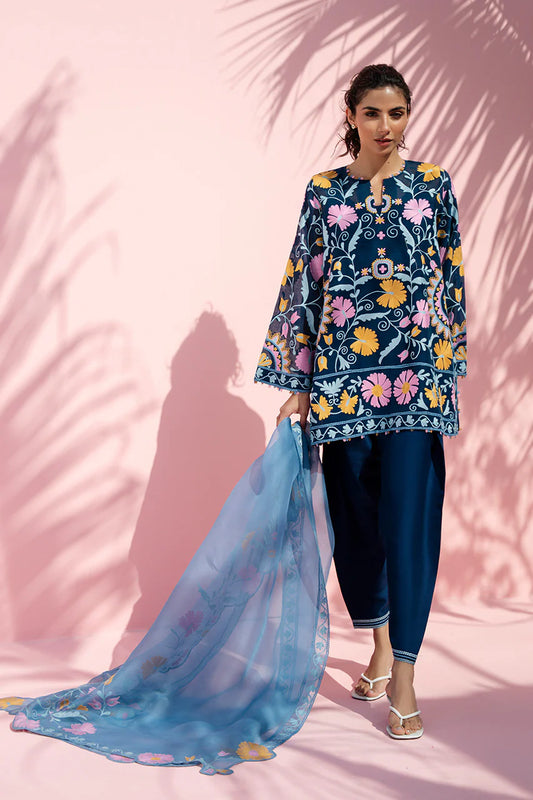 Woman in a floral embroidered outfit with a blue dupatta against a pink background