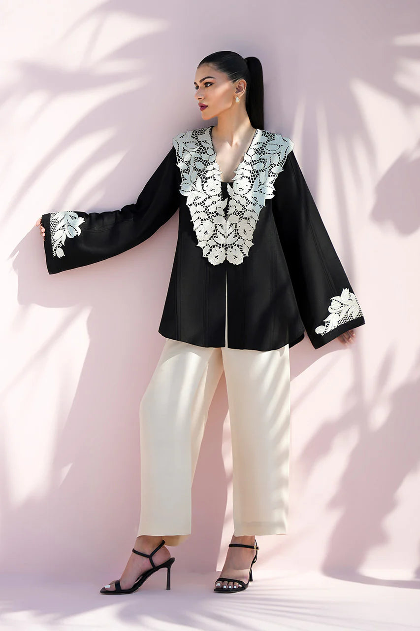 Woman wearing a black outfit with white embroidery against a light pink background