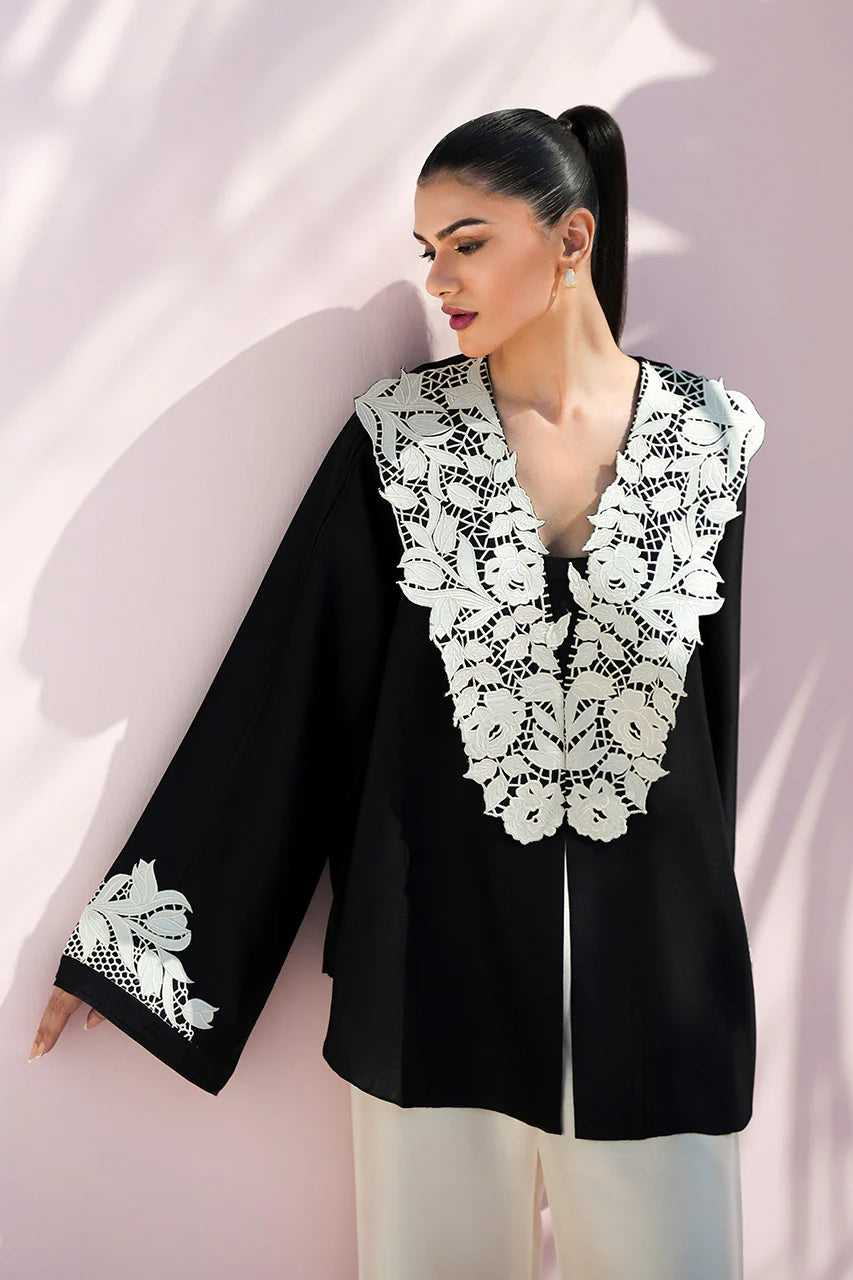 Woman wearing a black blouse with white lace details against a light pink background