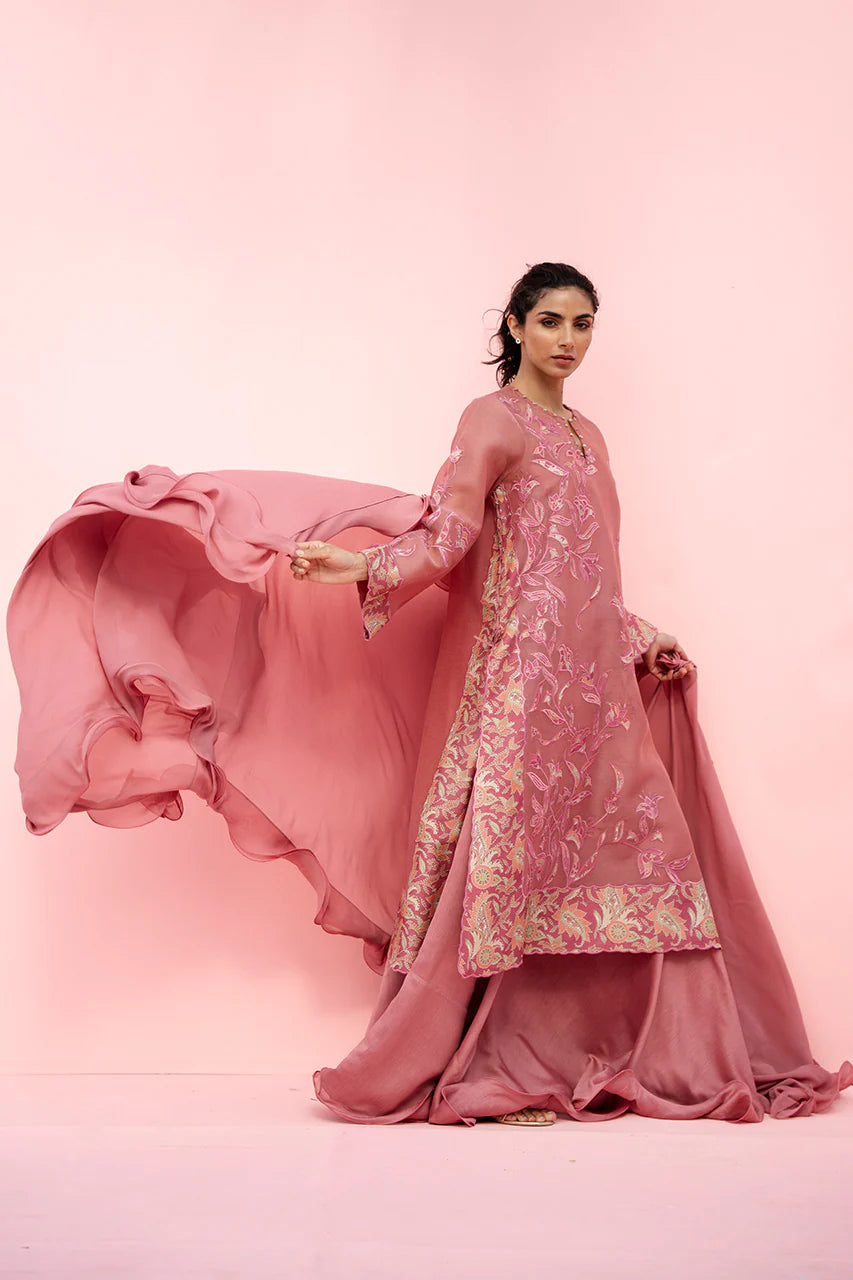 Woman in a pink traditional outfit with floral patterns against a pink background