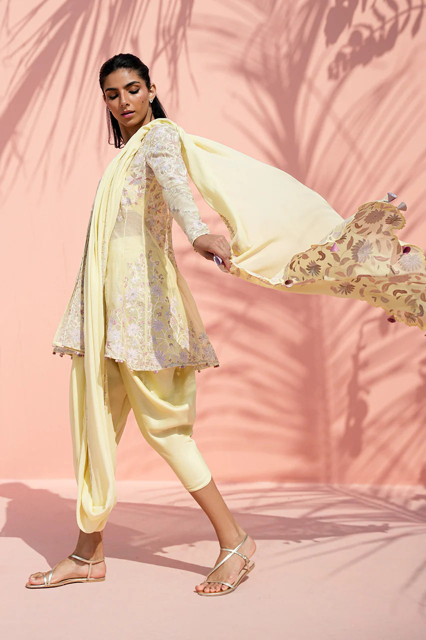 Woman in a light yellow traditional outfit with a floral dupatta against a pink background