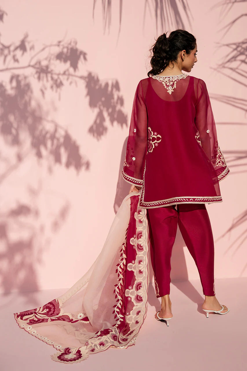 Woman in a red traditional outfit with white embroidery against a pink background