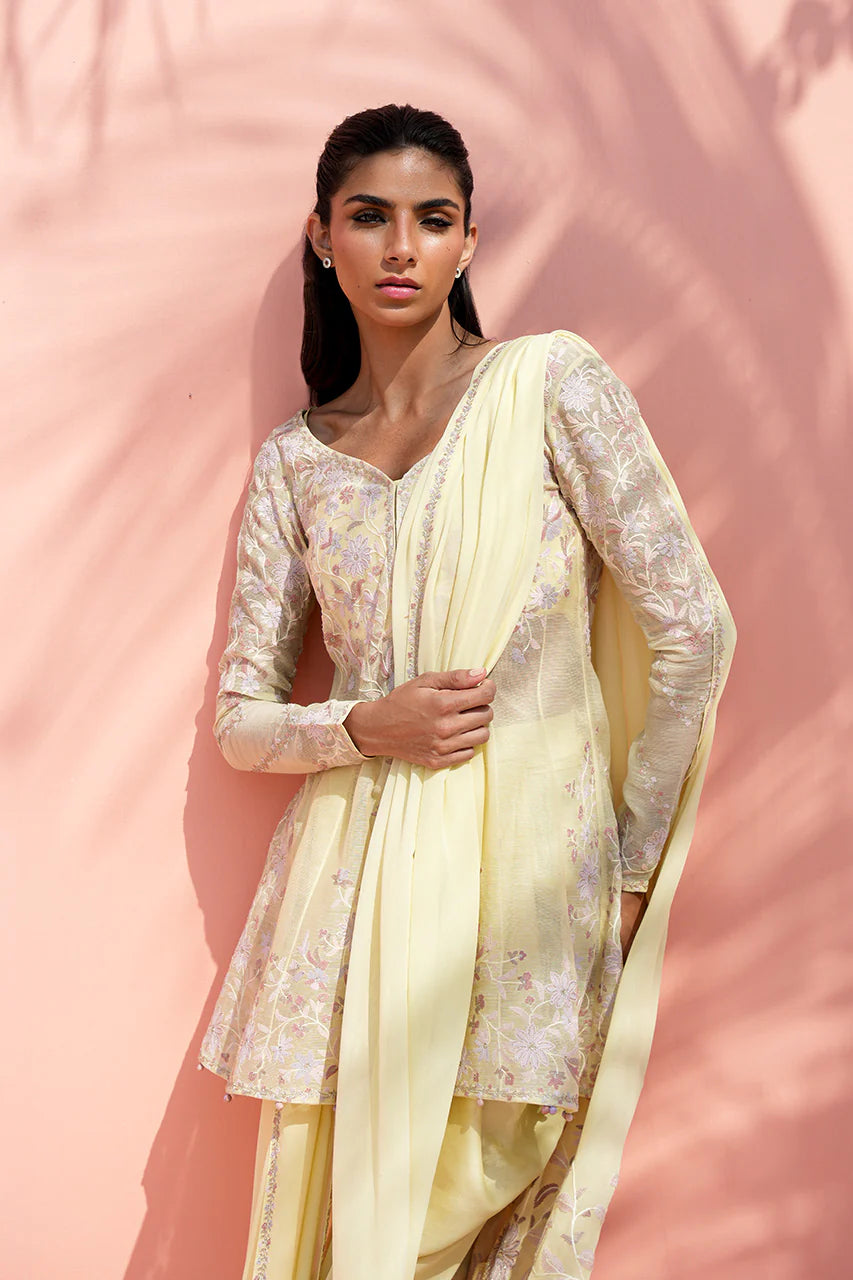 Woman wearing a light yellow traditional outfit with a floral pattern against a pink background
