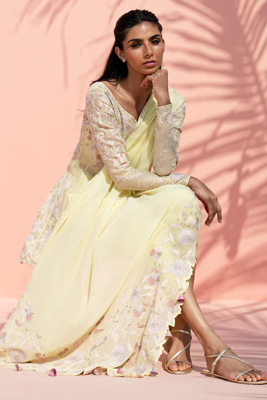 Woman in a light yellow floral saree sitting against a pink background