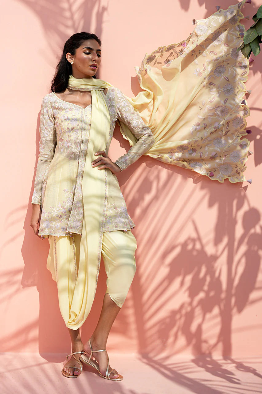 Woman in a light yellow traditional outfit with a flowing fabric against a pink background