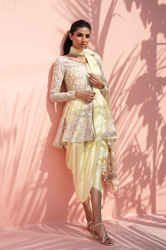 Woman in a light-colored traditional outfit against a pink wall with shadow patterns.