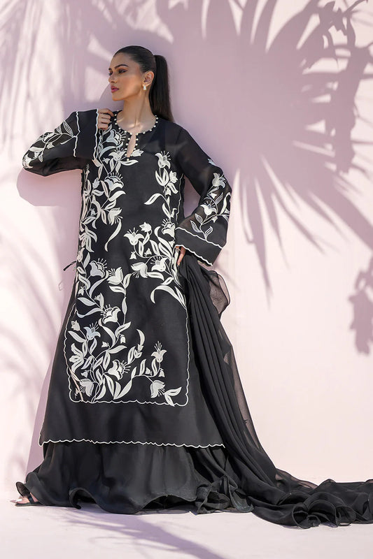 Woman wearing a black traditional outfit with white floral embroidery against a pink background