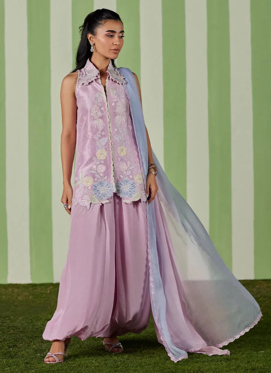 Woman in a pink traditional outfit with a matching dupatta against a green and white striped background