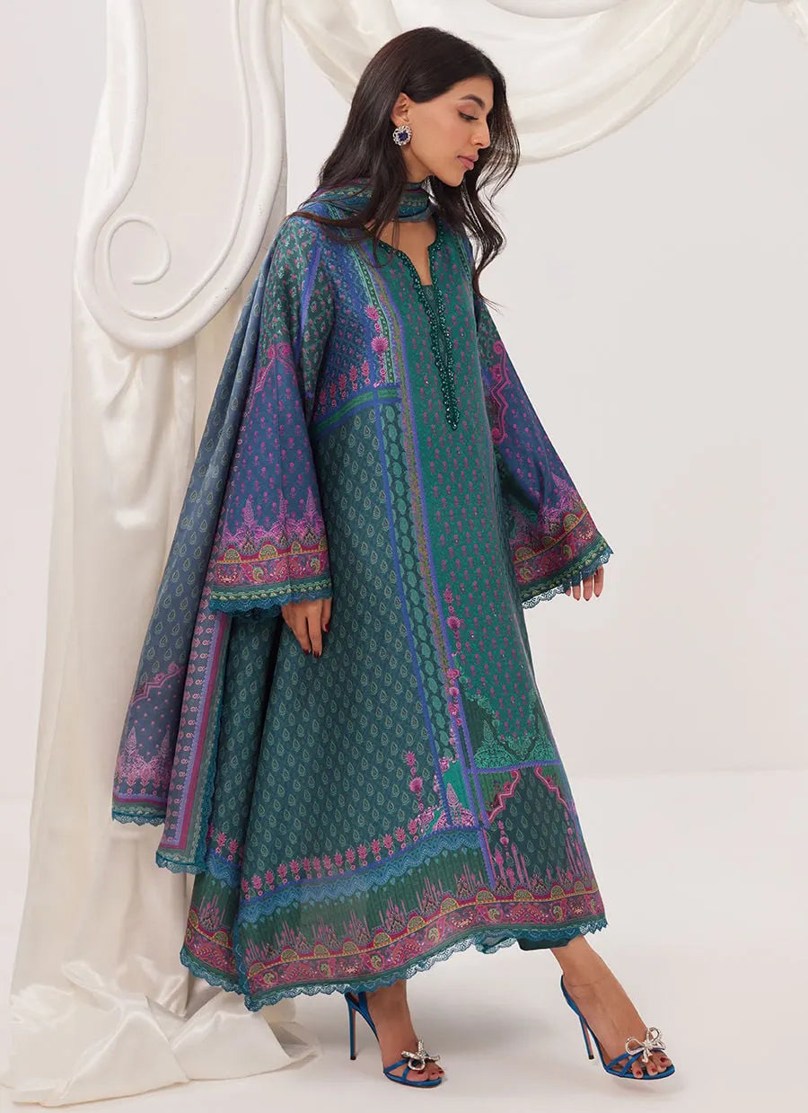 Woman wearing a patterned teal dress with long sleeves against a white background