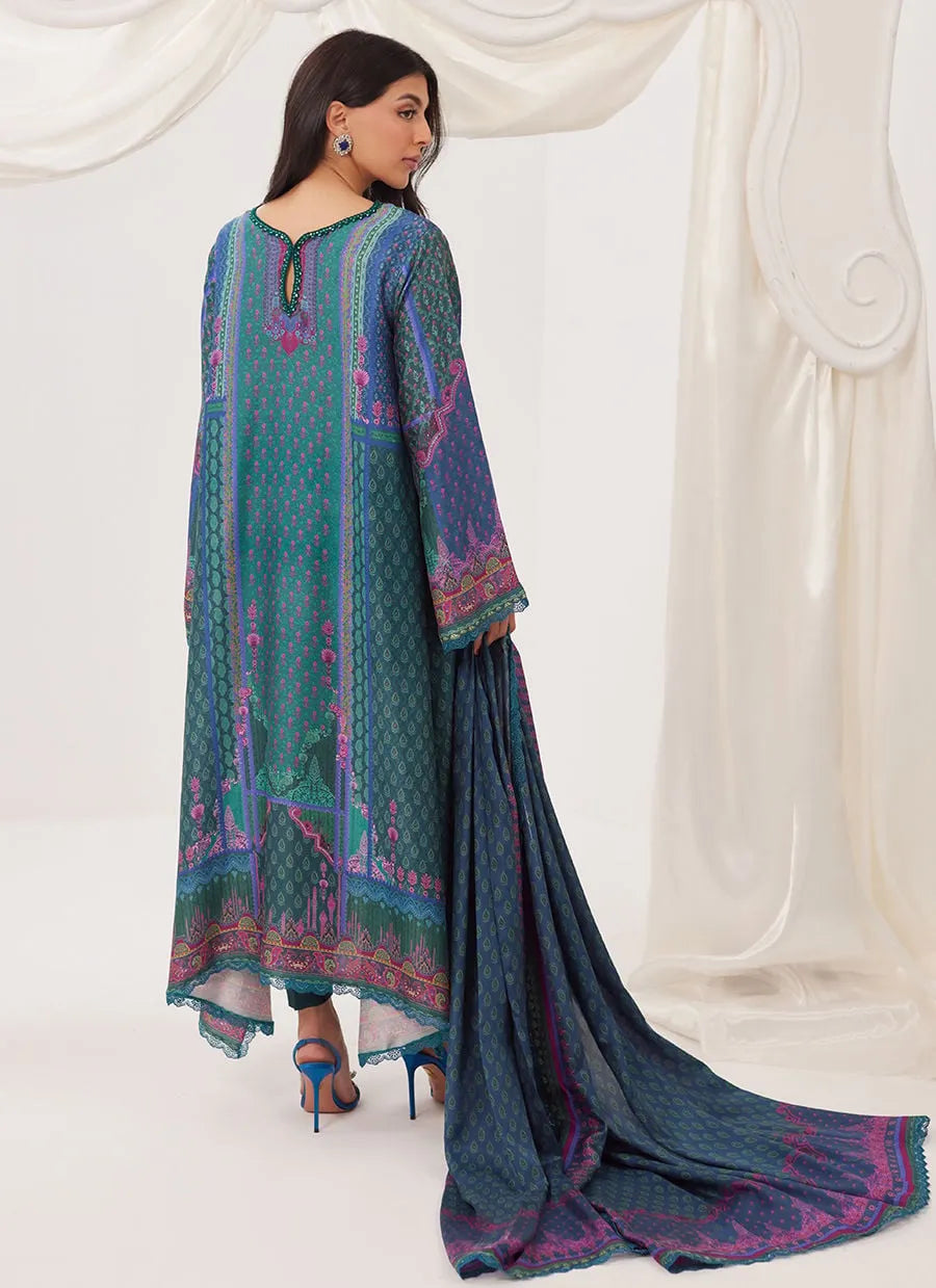 Woman wearing a blue and green embroidered traditional outfit with a white curtain background