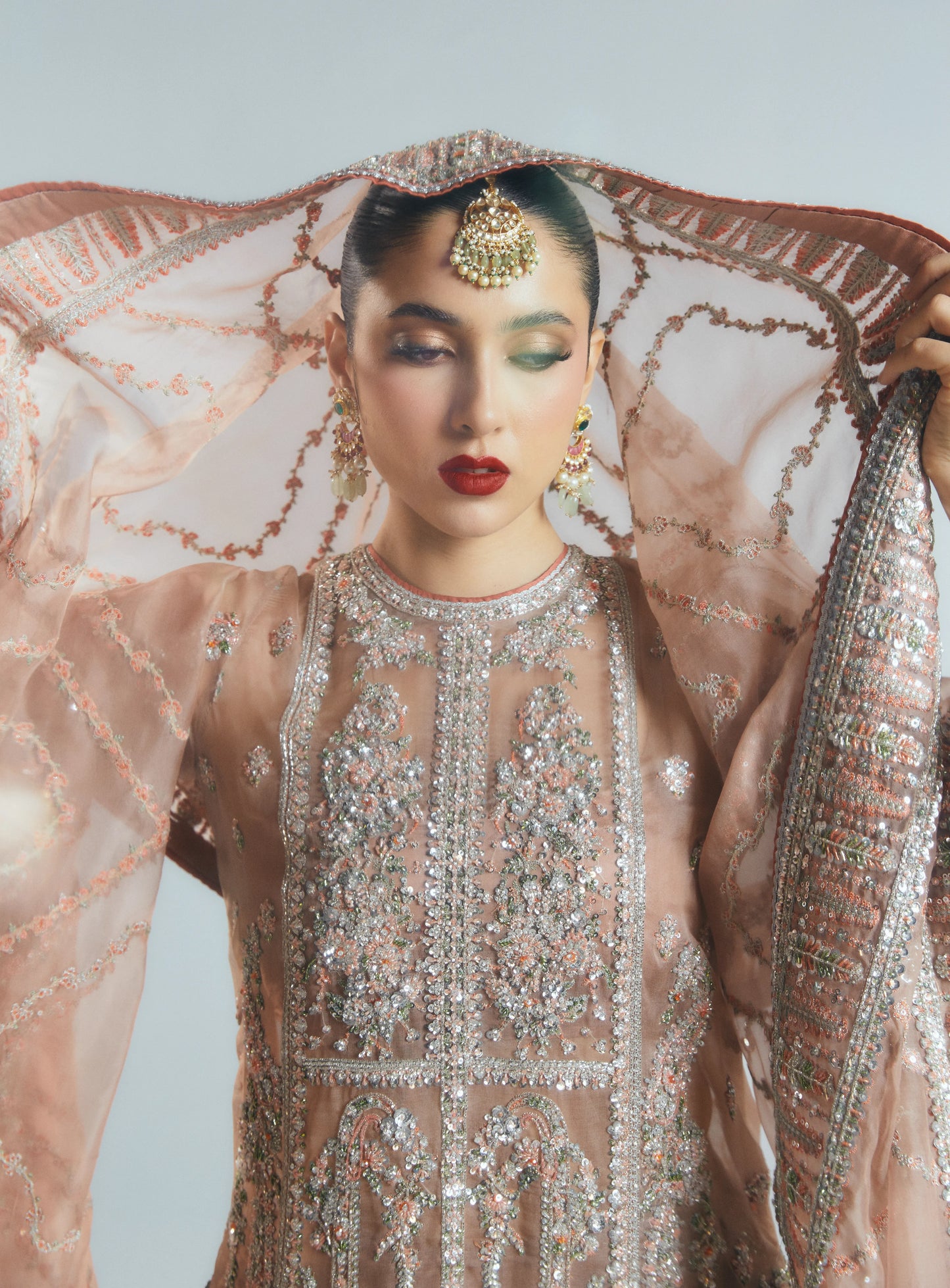 Woman in an ornate, embroidered traditional outfit with a sheer dupatta.