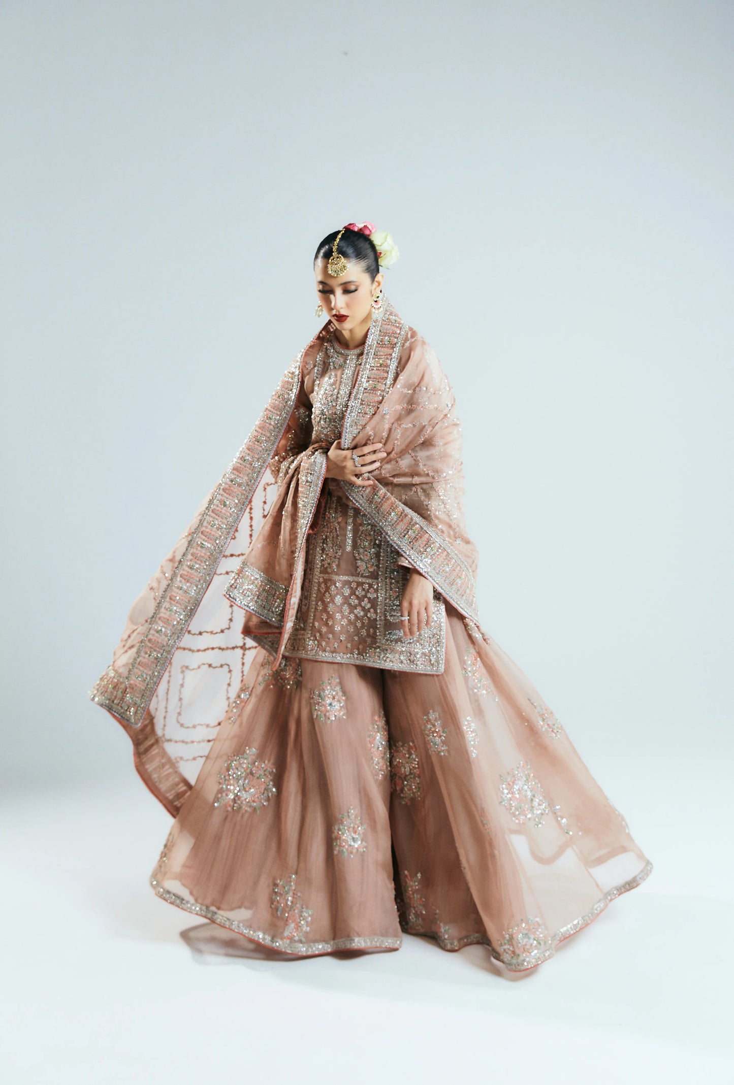 Woman in traditional pink embroidered outfit with dupatta on a white background