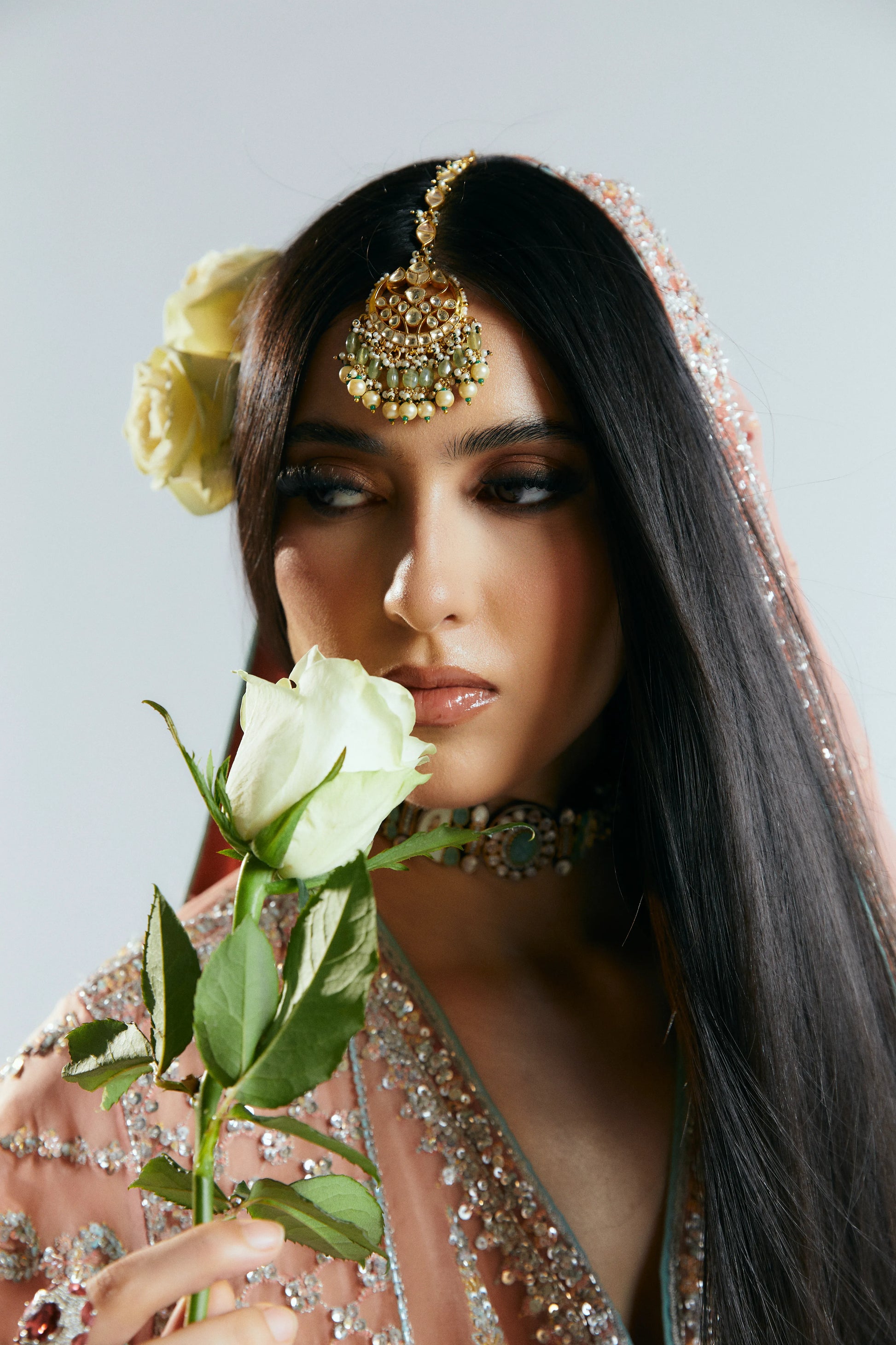 Woman in traditional attire holding a white rose against a plain background