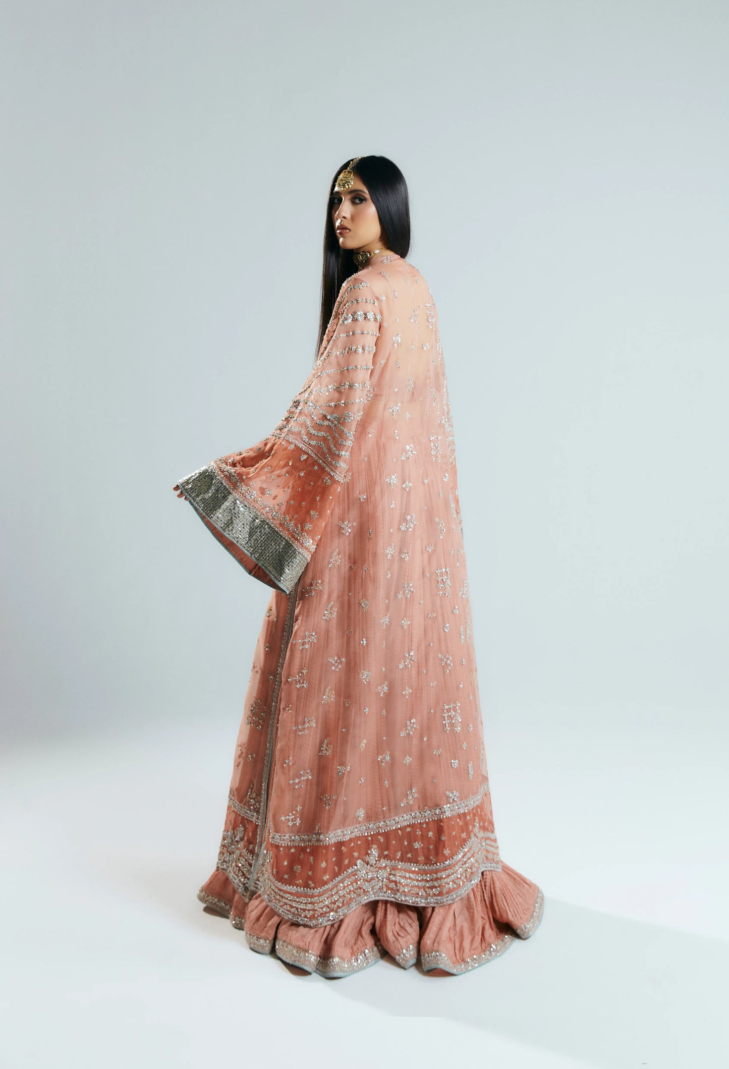 Woman wearing a traditional pink and orange embroidered outfit on a white background